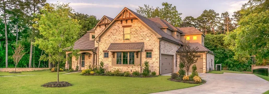 Two-story stone and brick house with a curved driveway surrounded by trees