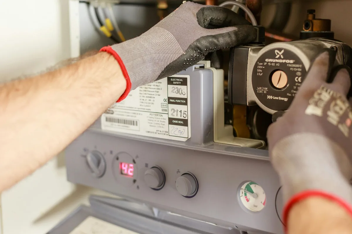 Gloved hands of a technician working on the circulator pump of a wall-mounted boiler