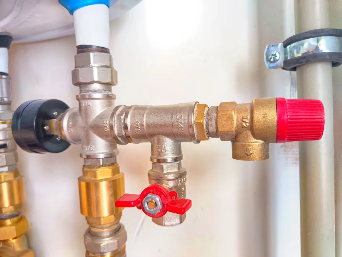Brass water pipe fittings with a red valve cap and a red shut-off handle