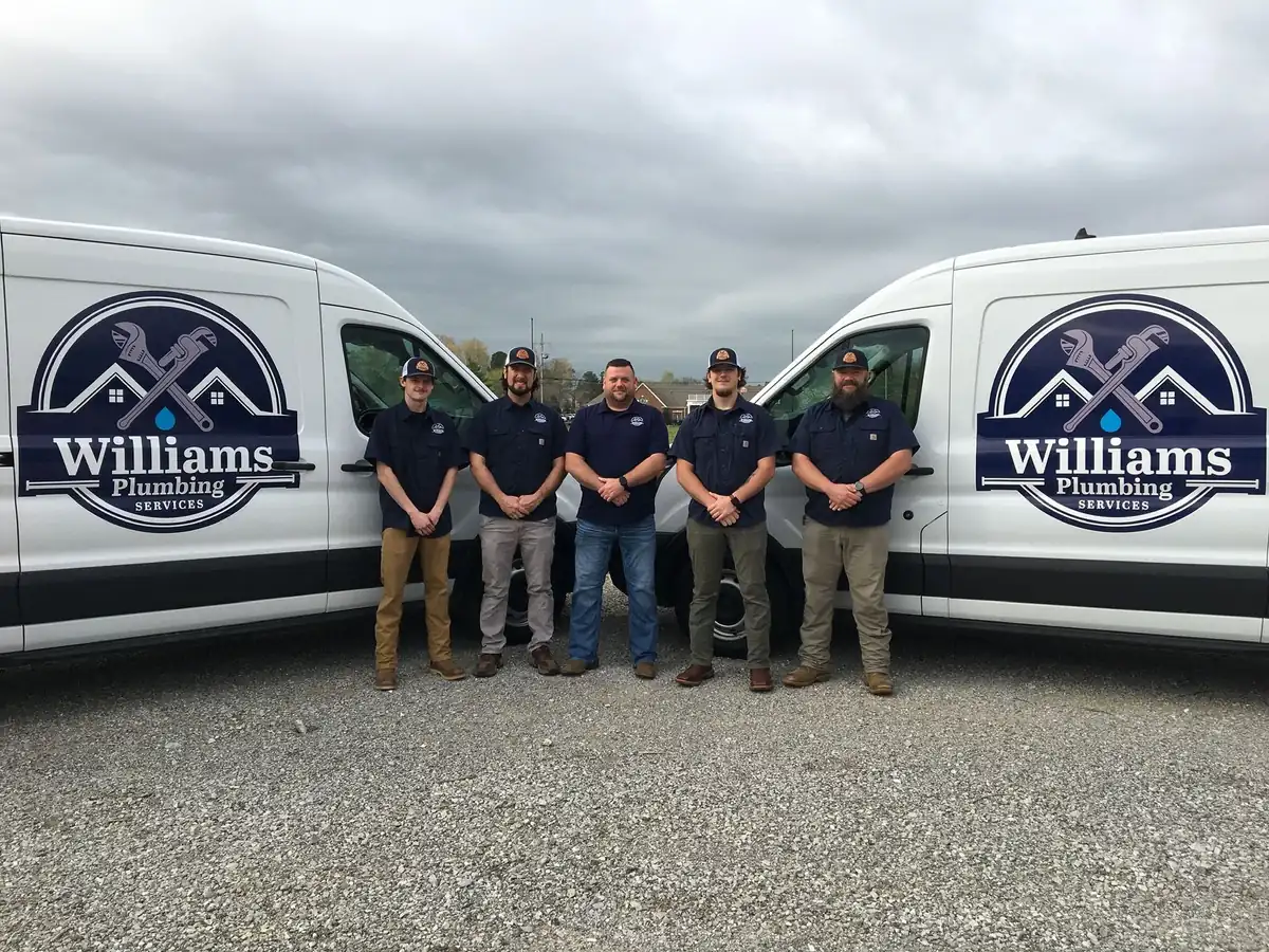 Five Williams Plumbing technicians standing between two branded white service vans