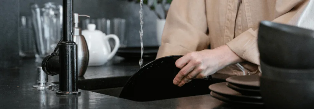 Person washing dishes at a dark kitchen sink