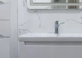 White bathroom vanity sink with a chrome faucet and a marble-look wall