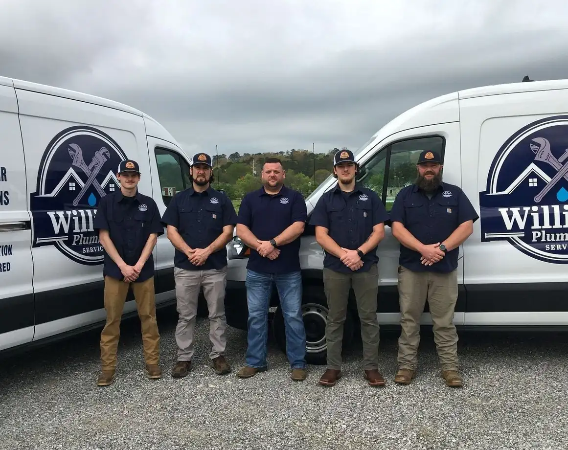 Five Williams Plumbing technicians in company uniforms between two service vans